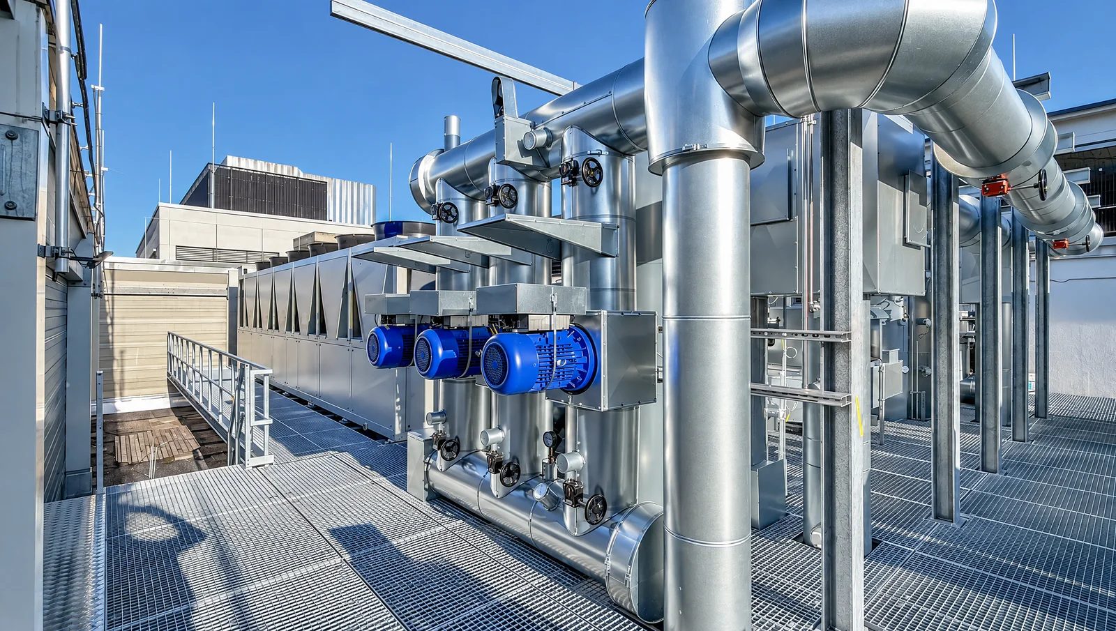 Kältetechnik auf dem Dach des NorthC-Rechenzentrums in München – drei blaue Pumpenmotoren an isolierten Kaltwasserleitungen, Aufstellung auf Gitterrost