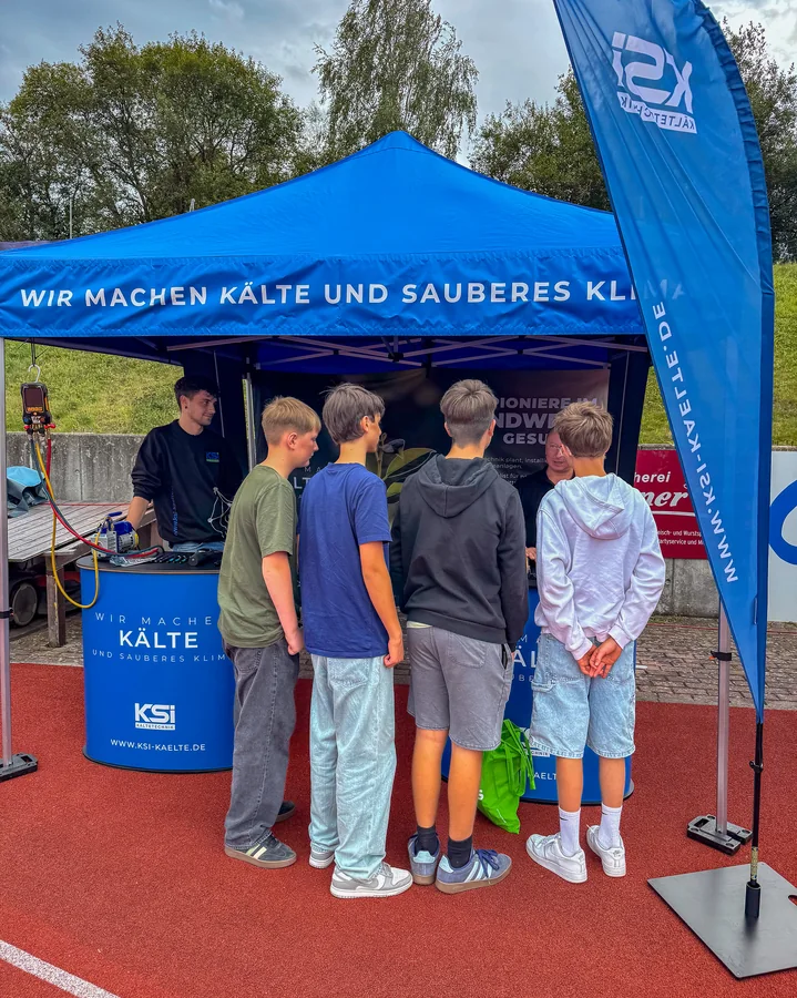 Four teenagers are standing at the KSI Kältetechnik exhibition stand under the blue pavilion in Plauen