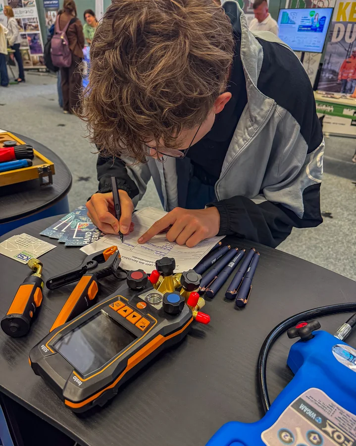 A teenager is making a note at the KSI Kältetechnik stand; a measuring device and tools are lying in front of him