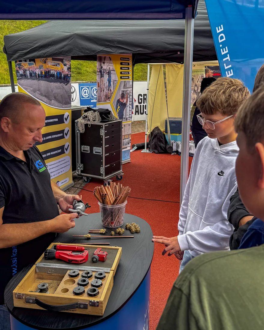 An employee from KSI Kältetechnik is showing two teenagers a tool at the exhibition stand in Plauen