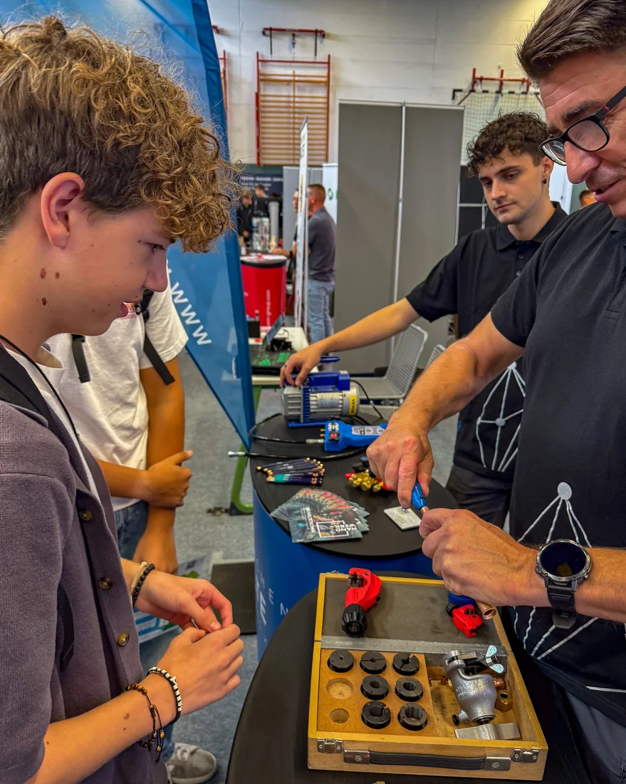 Two teenagers and two members of staff from KSI Kältetechnik at the tool table in the Reichenbach sports hall